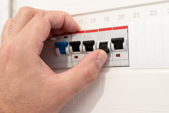 close-up of hand interacting with an electrical circuit breaker panel in German home. Person flips switch of fuse after electrical short. Maintenance and safety concept.