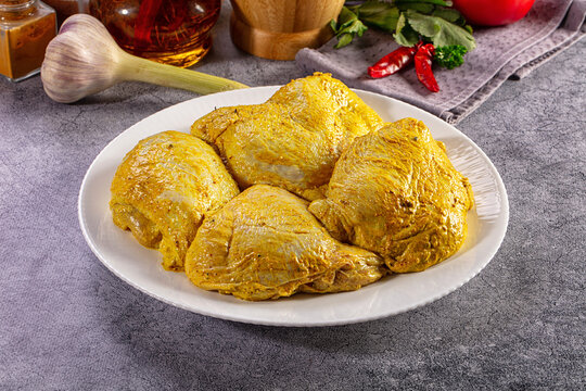 Raw chicken thighs in yellow turmeric marinade ready for cooking with spices