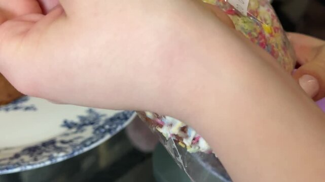 female hands gently removing a plastic wrap from the top of a traditional Easter bread. The glazed surface with white icing and decorative sprinkles is revealed, focusing on festive pastry.