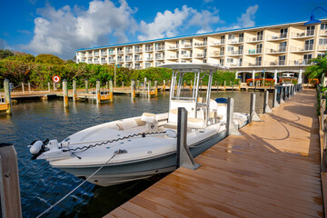 Obraz premium White motorboat docked at a wooden pier near resort building. High angle view of a powerboat moored at a boardwalk in a tropical marina canal.