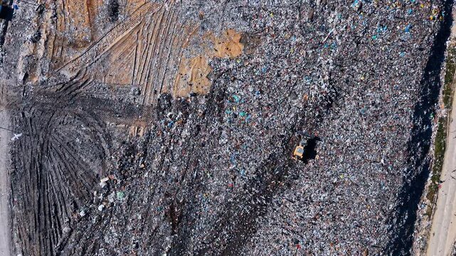 Top down aerial shot of bulldozer working at landfill site. Vertical view of heavy machinery moving waste with seagulls flying above