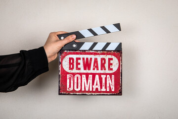 Naklejka premium Beware Domain Warning Sign with Film Clapperboard Held by Hand