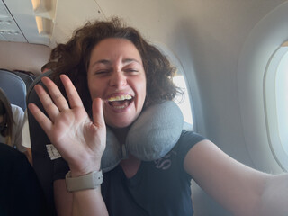Naklejka premium Happy passenger young woman is flying in plane. Smiling girl sitting in airplane near window going on trip vacation travel. Traveling female inside plane enjoying flight. Traveling girl