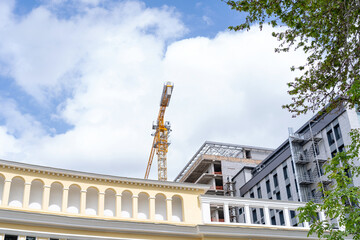 Obraz premium A construction tower crane operates against the backdrop of an unfinished building and a blue sky. Concept: Urban construction pollutes the air