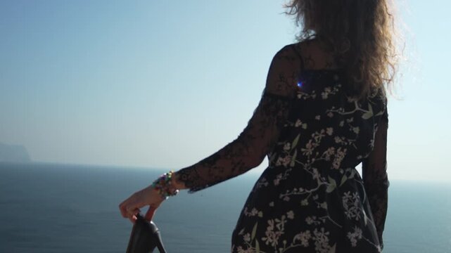 Woman, cliff, heels. Standing on a dramatic edge, holding high heels, she looks out at the vast ocean view.