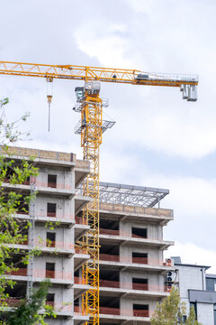 A construction tower crane operates against the backdrop of an unfinished building and a blue sky. Concept: Urban construction pollutes the air