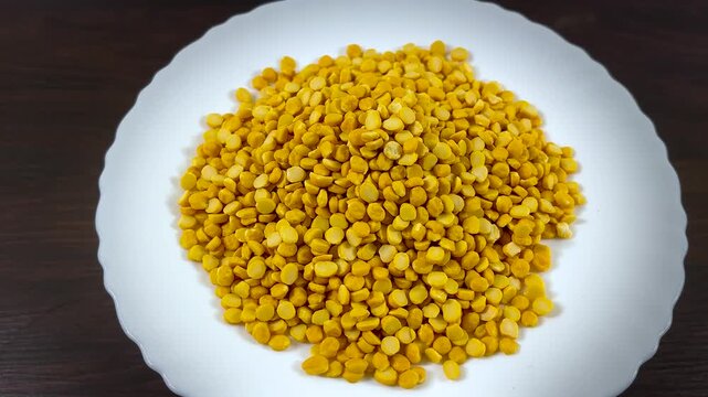 Chana dal yellow split chickpeas on white ceramic plate, organic dried pulses and legumes for healthy cooking, raw protein rich indian lentils