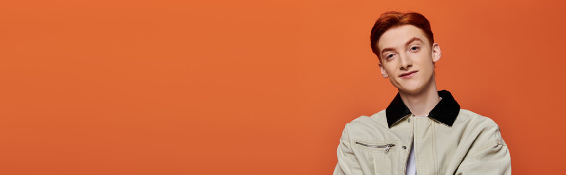 Handsome young man with red hair poses confidently against a vibrant orange background