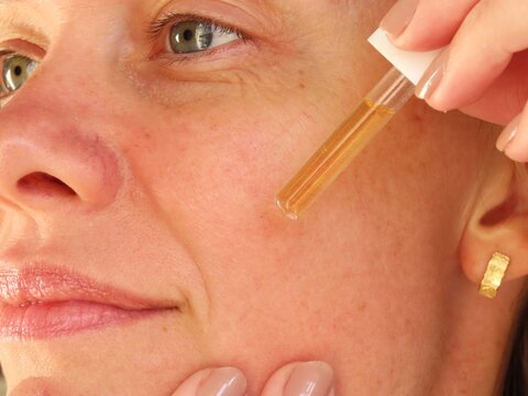 Closeup of woman applying vitamin C serum on her face. Woman in her 40s doing her beauty routine. Skin care routine.