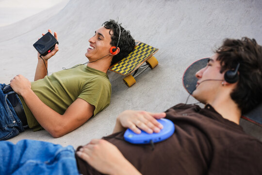 Two young friends listening music with cassette player and cd player - New trend people lifestyle using vintage analog devices - Focus on left man face