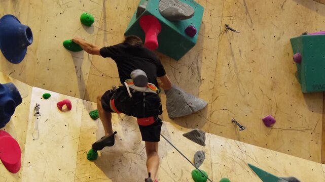 Young athlete shows astonishing dexterity as climbs up rock face. Climber demonstrates agility on indoor climbing wall slow motion