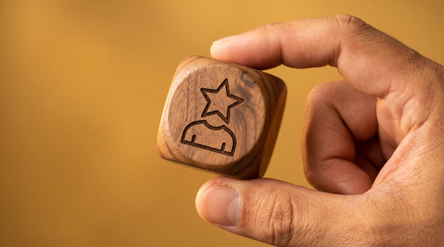 A wooden cube with a star-crowned person silhouette icon held by hand on a rich gold background, symbolizing personal branding and influence.