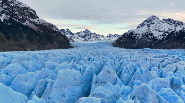 Aerial view of the Perito Moreno Glacier's icy expanse, where towering snow-capped mountains meet a frozen river of blue, El Calafate, Argentina.