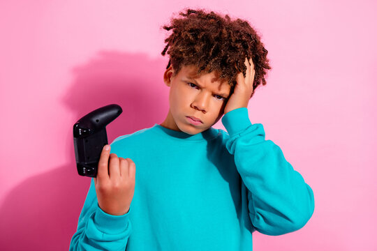 Frustrated boy holding a broken game controller with a confused expression against pink background, gaming disappointment and childhood emotion in a colorful studio portrait