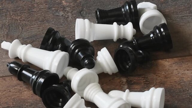 Scattering of black and white chess pieces on a wooden table during afternoon light