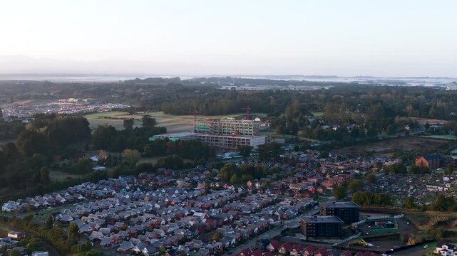 Aerial drone footage at sunrise showing the construction site of the future hospital in Puerto Varas, Chile, with cranes and morning light.