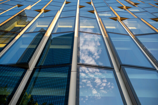 Modern building architecture with glass facade windows and urban skyline where clouds reflection mixes with golden lines suggesting premium corporate brand