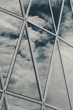 Urban skyline reflected in clouds reflection across glass windows on modern facade building architecture showing diagonal lattice lines and detail
