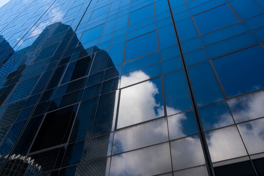 Urban skyline and clouds reflection bend across glass windows of modern facade building architecture forming surreal curves and dramatic abstract geometry