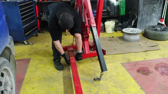 Technician installs construction for hanging parts. Specialist touches metal crane legs with hands before lifting engine off floor