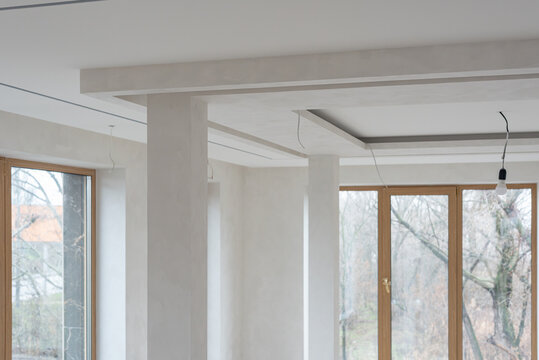 Unfinished celling in minimalist empty white living room interior Newly renovated interior space with decorative plaster walls and structural columns showing modern apartment