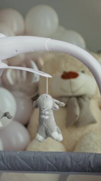 Close-up of a baby crib mobile with plush animal toys hanging above a large teddy bear and pastel balloons