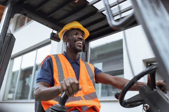 Portrait of a worker operator in a metal warehouse wearing personal protective gear sits in a forklift to transport and load heavy materials.