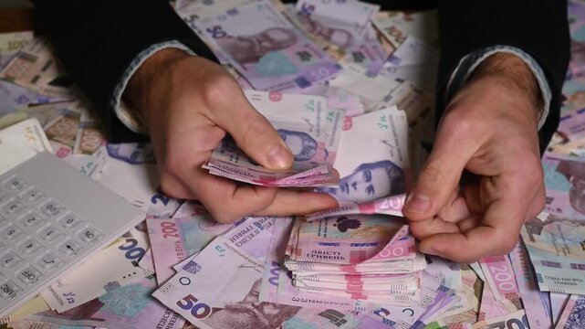 Businessman flips through Ukrainian hryvnia banknotes showing finance, earnings and monetary success. Counting process of paper money representing investment, financial planning in Ukraine.