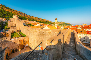 Obraz premium Golden hour panorama of Dubrovnik's historic fortifications and old port at dusk, featuring sunlight on ancient stone walls and Mediterranean architecture in Croatia