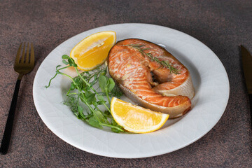 Baked trout steak with lemon, rosemary and garlic on white plate © Anzhela