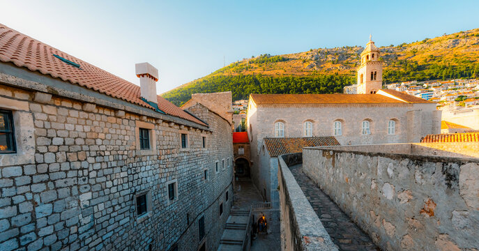Golden hour panorama of Dubrovnik's historic fortifications and old port at dusk, featuring sunlight on ancient stone walls and Mediterranean architecture in Croatia