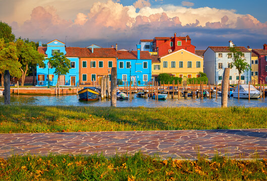 Colorful houses of Burano island in Venice, Italy. Motorboats parked along the channel and walking path in the grass. Venezia evening sunset view at street old European fisherman village.