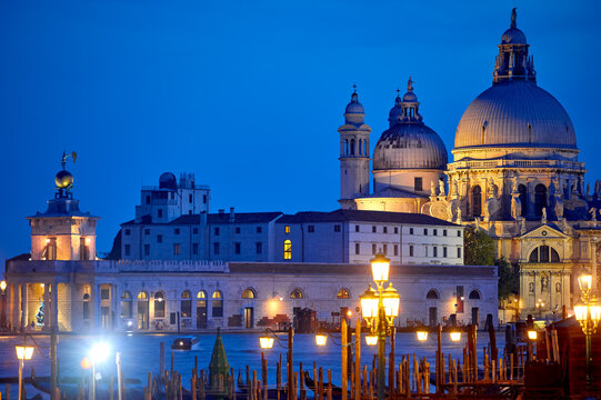 View at Cathedral of Santa Maria della Salute in Venice old town, Italy. Nighttime panorama of antique medieval building with dome at banks of Grand Canal. View from canal with lanterns.