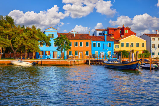 Colorful houses of Burano island in Venice, Italy. Motorboats parked along the channel. Venezia evening sunset view at street old European fisherman village.