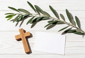 Fototapeta premium Small wooden cross lying next to an olive branch and a blank white card on a rustic white wooden background, religious concept for Easter, peace, and prayer