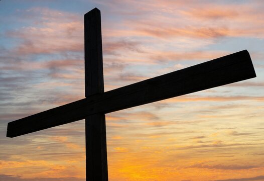 Wooden cross standing against a vibrant sunrise sky with orange and pink clouds, symbolic of faith and hope for Christian religion and spiritual meditation