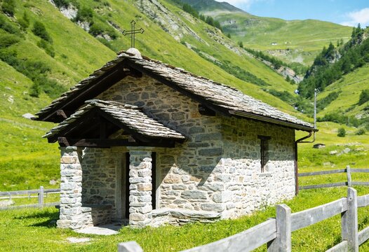 Small stone chapel with iron cross standing in a green mountain valley, traditional alpine architecture and religious heritage for travel and spiritual peace in nature
