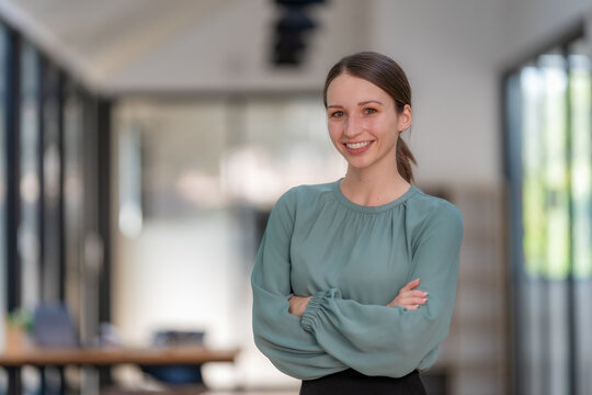 Confident young businesswoman smiling with arms crossed in modern office, leadership and success concept.