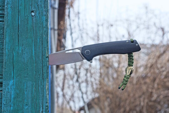 A single folding knife with a black handle sticks out of the green wooden wall of a house on a daytime street