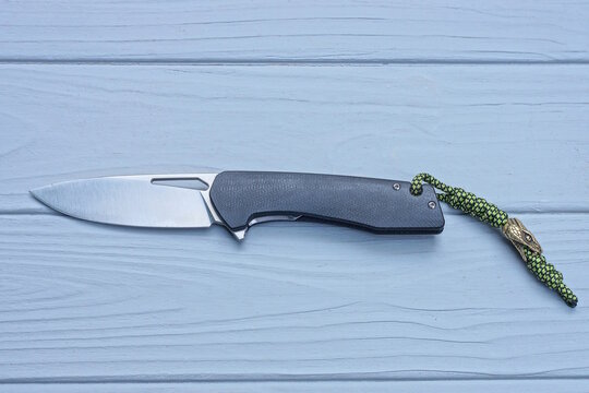 one folding knife with a black handle and a white blade lies on a gray wooden table