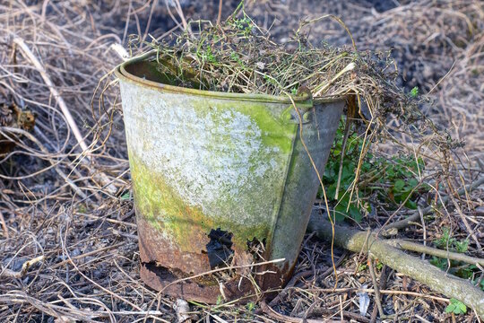 one old broken rusty grey brown bucket with a hole on the ground on the day street