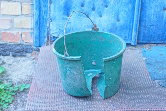 One old broken green plastic bucket stands on the brown floor on the daytime street