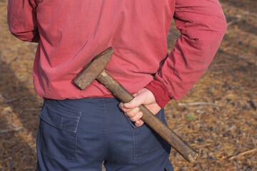 Obraz premium a one man criminal in red blue clothes holds a large brown hammer in his hand behind his back on the street