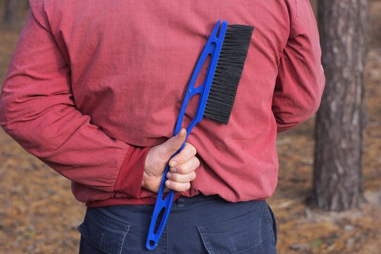 one man in red clothes holds a plastic large blue black brush in his hand behind his back on the street