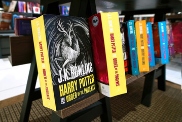 Naklejka premium Minsk, Belarus. Apr 12, 2026. Row of colorful Harry Potter fantasy novels published by bloomsbury arranged on wooden display stand inside retail book shop with blurred white bookshelves in background