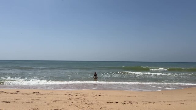 Young woman raising hands on beach. Summer holidays at tropical island. Small waves crashing on shore. Relaxation concept 