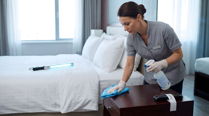 Obraz premium Housekeeper disinfecting hotel room furniture with UV light and spray
