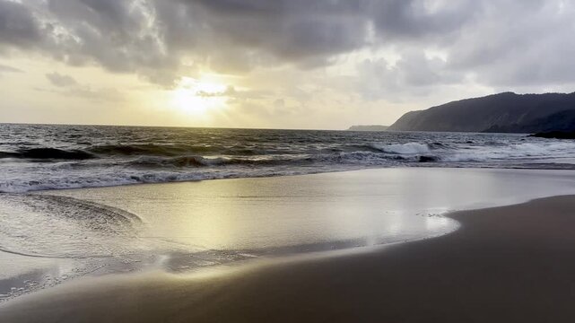 Wide angle seascape of Goa beach with hills at sunset and dramatic clouds