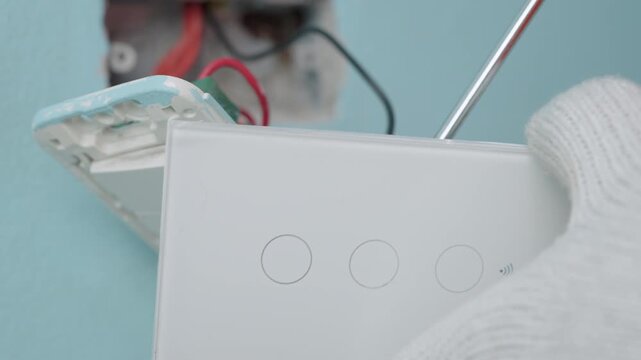 Technician uses a screwdriver to installing modern switch, touch or smart phone-controlled on-off light, Smart Home.