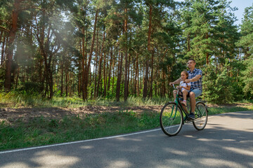 Fototapeta premium Young father with his little daughter on bicycle in summer sunny forest